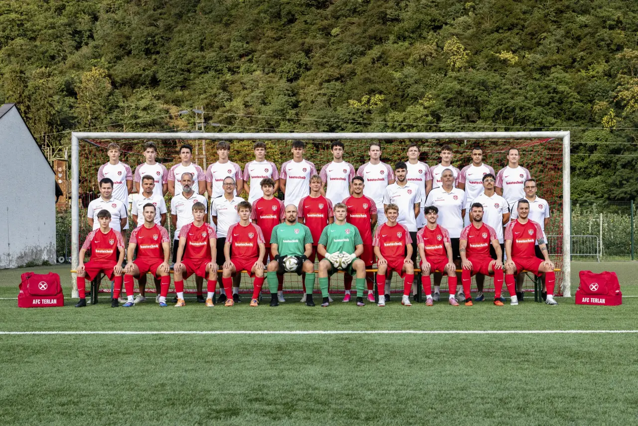 Mannschaftsfoto des AFC Terlan mit Spielern in Rot und Weiß vor einem Tor, davor Trainer und Torhüter in Grün, im Hintergrund bewaldeter Hang.