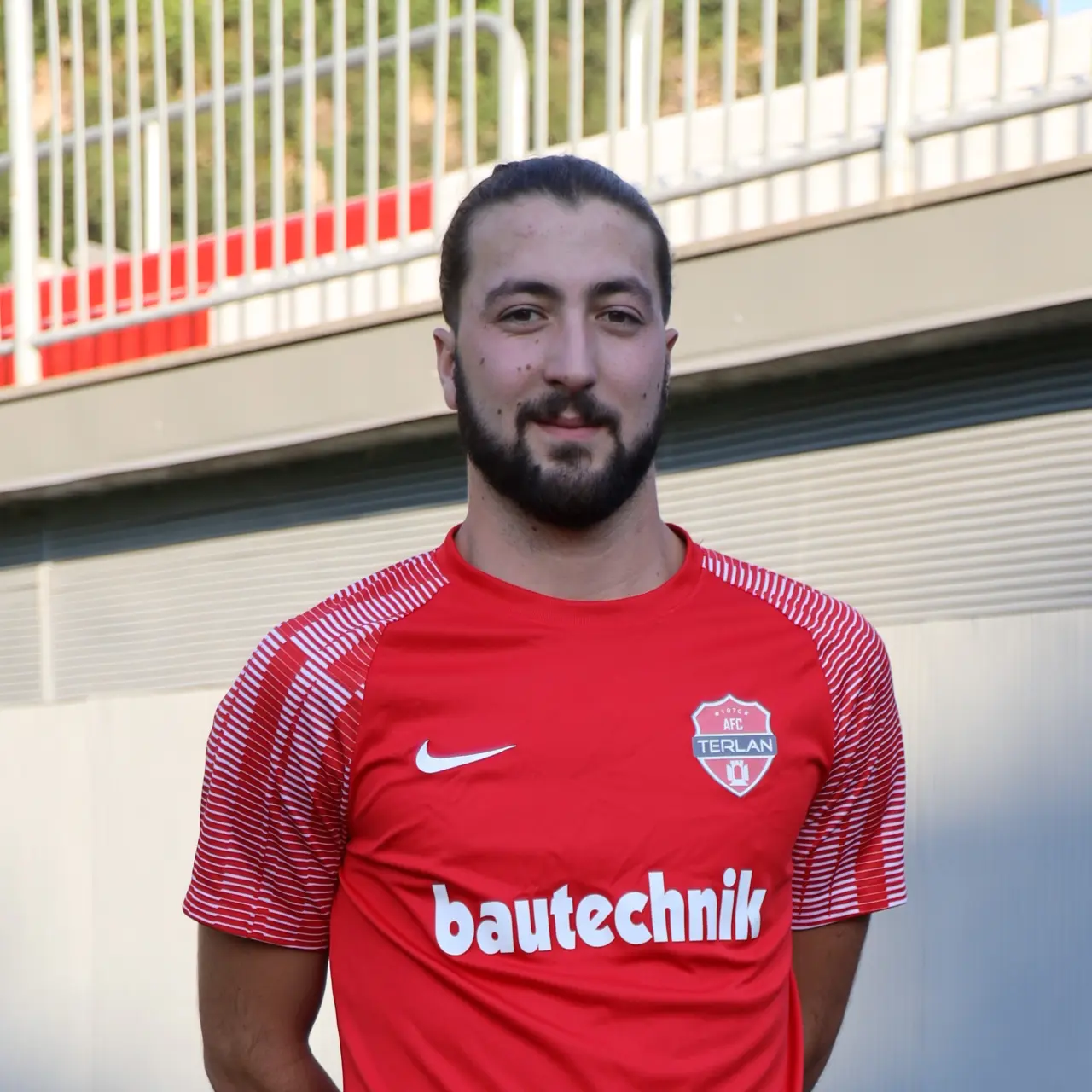 Porträt von Felix Lintner im roten Trikot des AFC Terlan mit Bautechnik-Sponsor, vor einer Tribüne stehend.