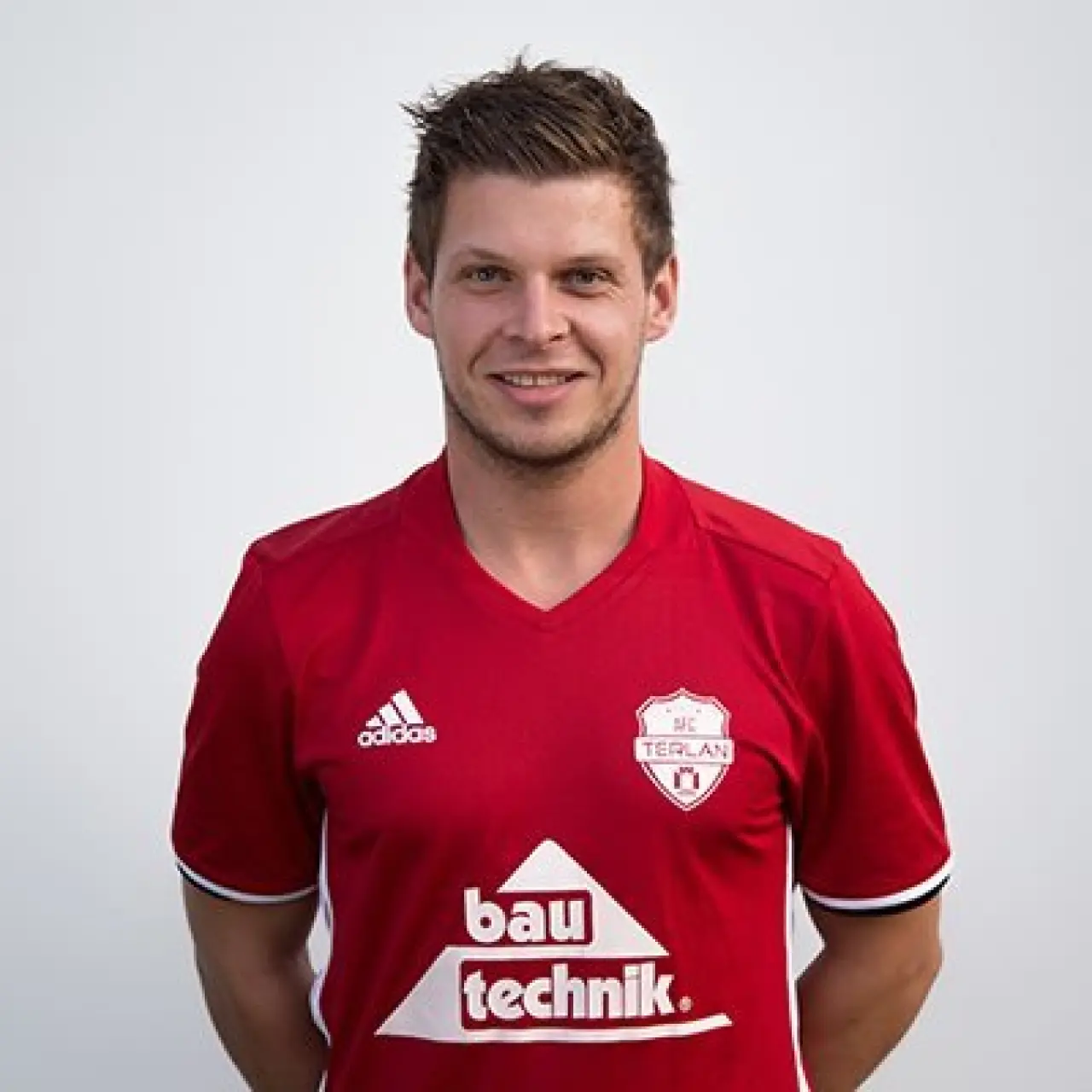 Porträtfoto eines lächelnden Spielers im roten Trikot des AFC Terlan mit Adidas- und Bautechnik-Sponsorlogo vor hellem Hintergrund.