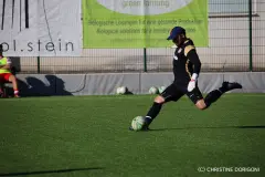 Torwart im schwarzen Trikot schießt auf dem Kunstrasen einen Ball ab, im Hintergrund Banner und Ersatzbälle am Spielfeldrand.