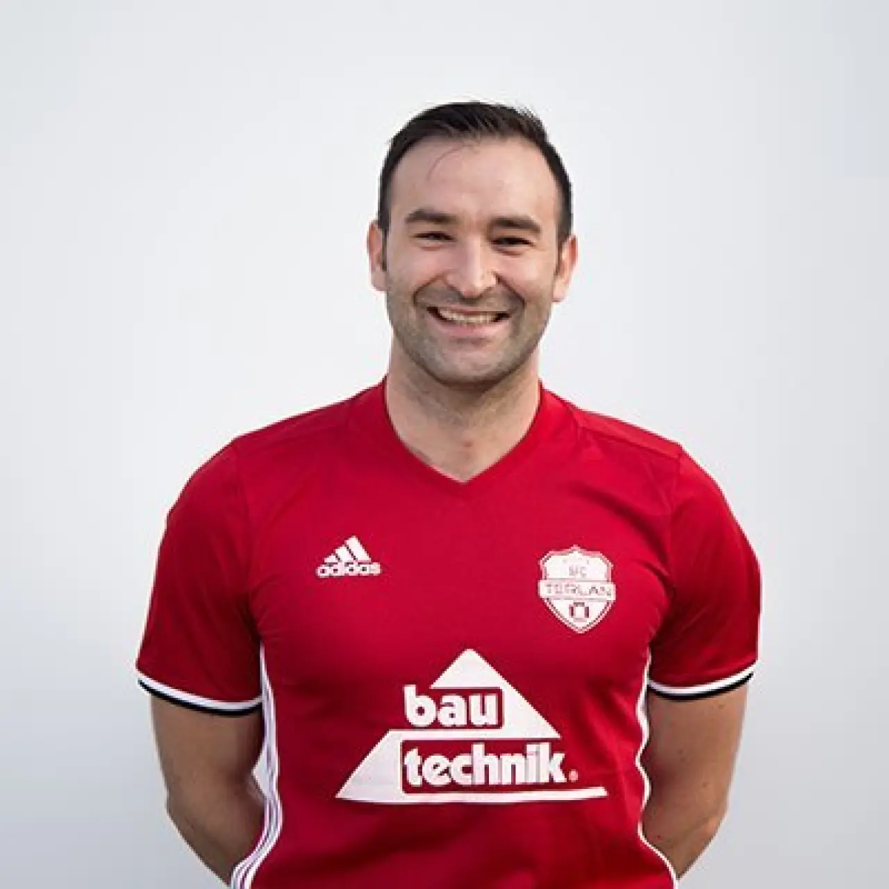 Porträt eines lächelnden Mannes im roten Trikot des AFC Terlan mit dem Sponsorenlogo Bautechnik vor hellem Hintergrund.