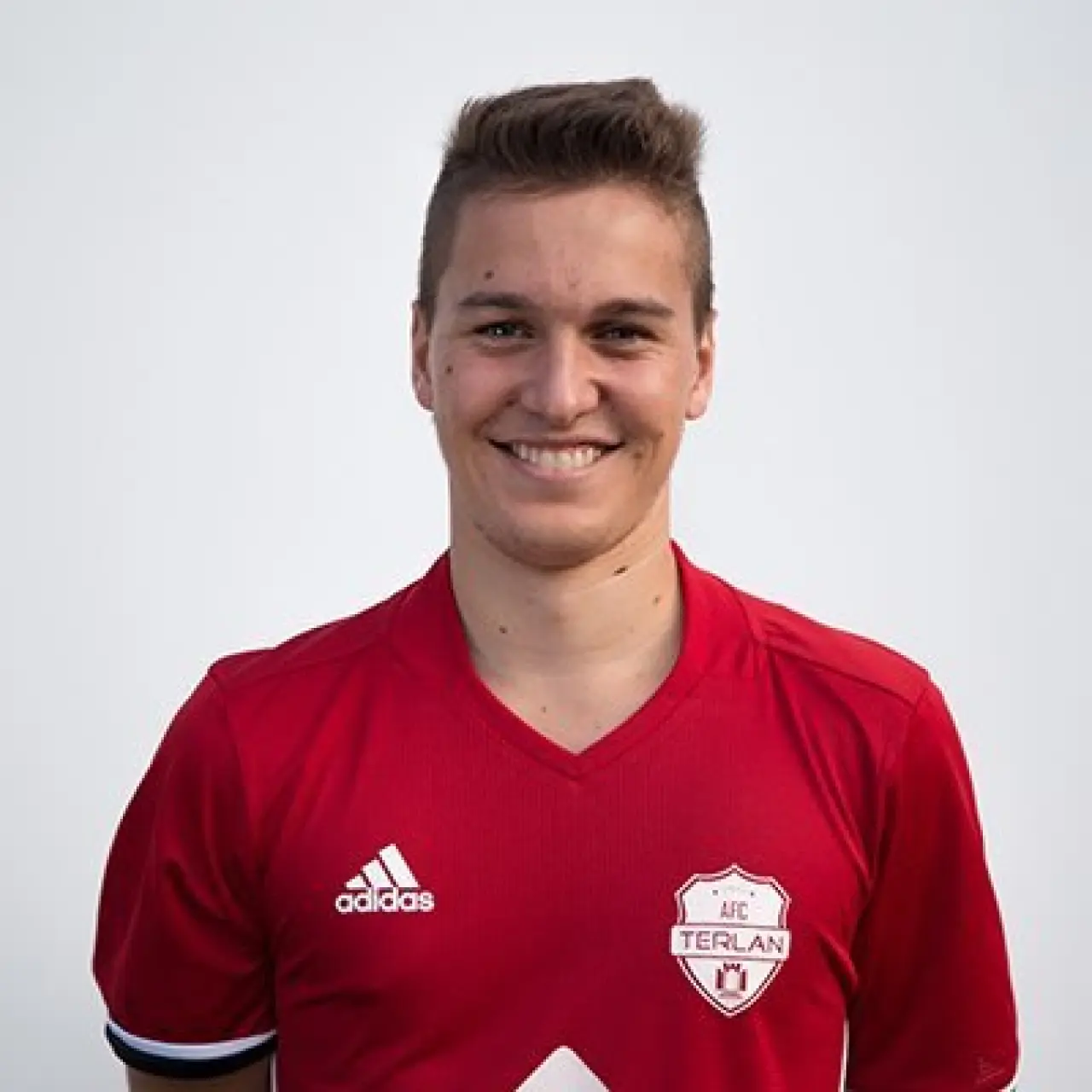 Porträt von Thomas Albenberger im roten Trikot des AFC Terlan, lächelnd vor hellgrauem Hintergrund.