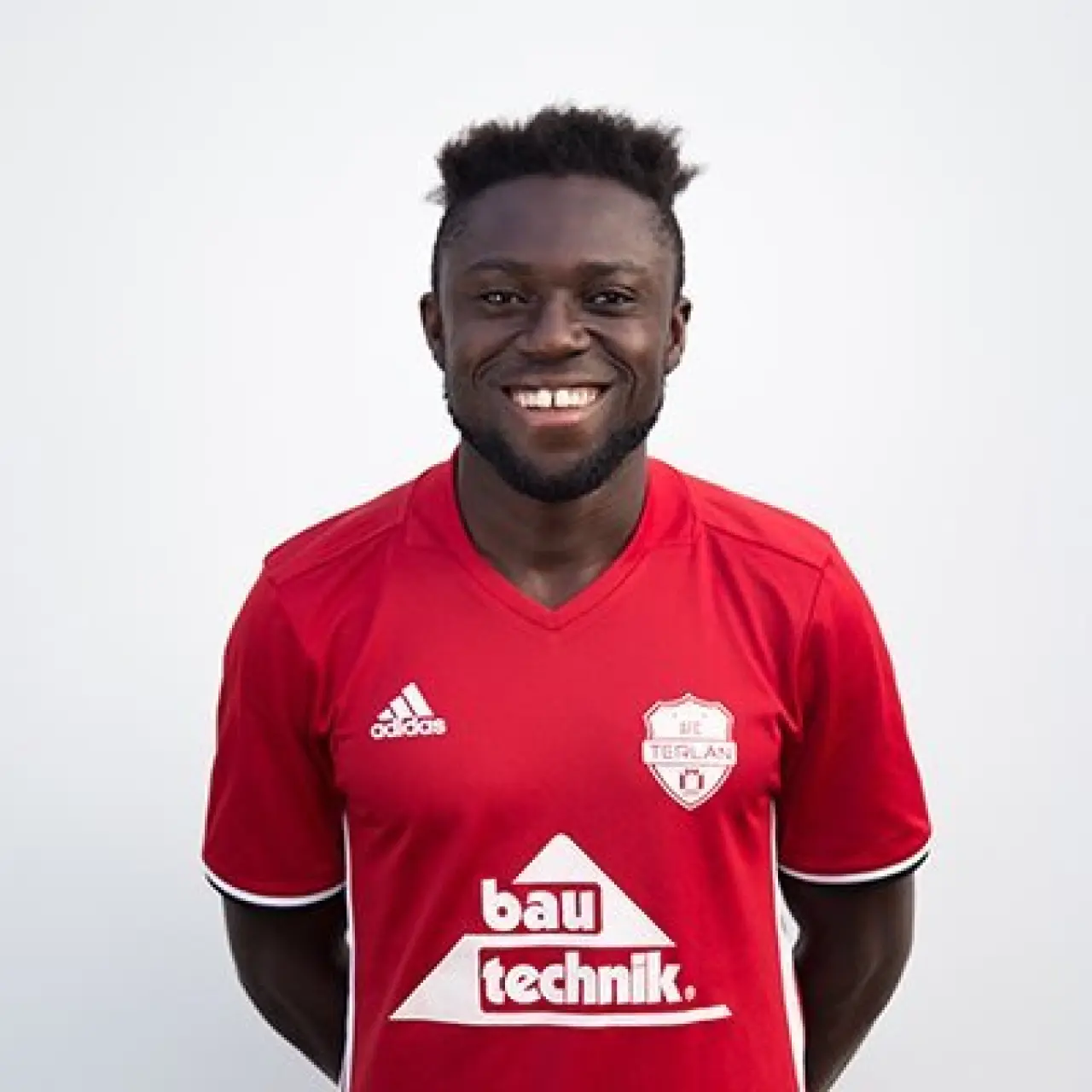 Lächelnder Spieler des AFC Terlan im roten Trikot mit Bautechnik-Sponsor vor hellem Hintergrund, Porträtfoto für den Mannschaftsauftritt.