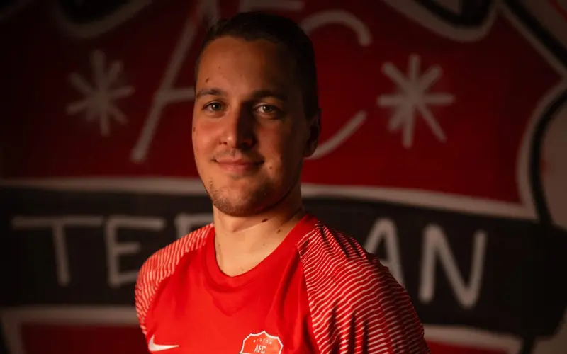 Porträt eines Spielers des AFC Terlan in roten Trikot mit Vereinswappen und Bautechnik-Sponsor vor dem Vereinslogo an der Wand.