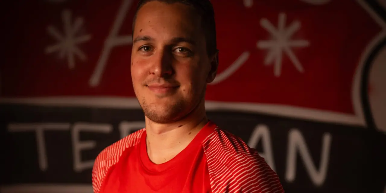 Porträt eines Spielers des AFC Terlan in roten Trikot mit Vereinswappen und Bautechnik-Sponsor vor dem Vereinslogo an der Wand.