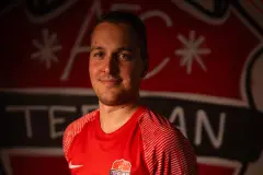 Porträt eines Spielers des AFC Terlan in roten Trikot mit Vereinswappen und Bautechnik-Sponsor vor dem Vereinslogo an der Wand.