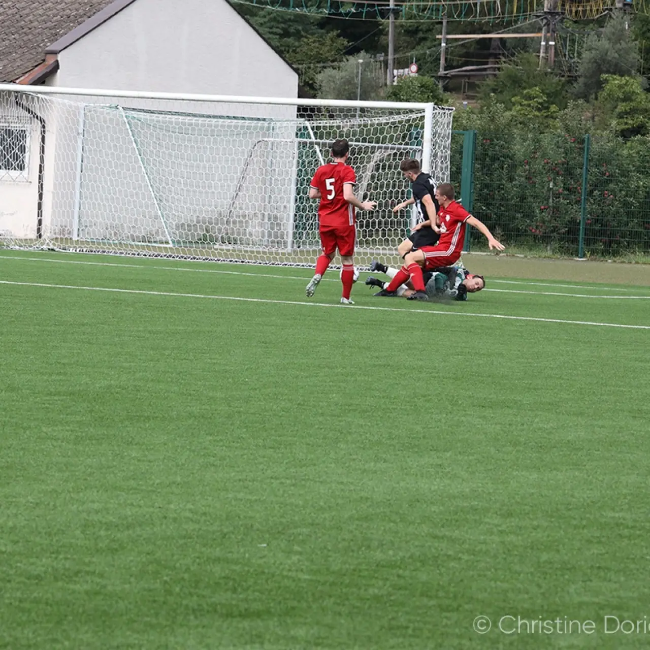 Spielszene: Rot gekleidete Spieler des AFC Terlan und ein Gegenspieler in Schwarz kämpfen am Boden vor dem Tor um den Ball, daneben Mitspieler.