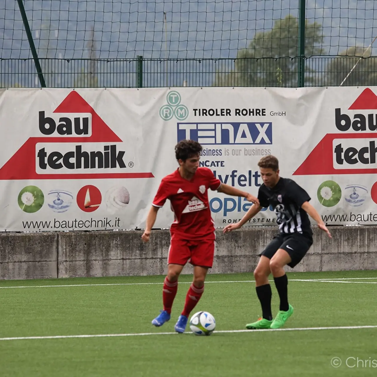 Zwei Jugendspieler kämpfen um den Ball auf dem Kunstrasen, im Hintergrund Werbebanden von bautechnik.