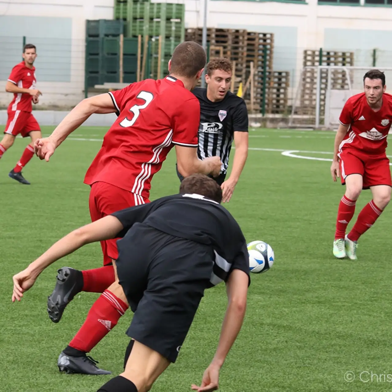 Spielszene: Ein Spieler in Rot mit der Nummer 3 und ein Spieler in Schwarz kämpfen um den Ball auf einem Kunstrasenplatz.