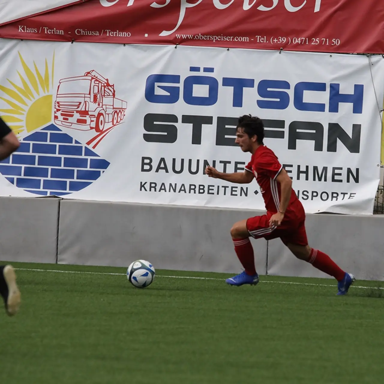 Spieler in roter Vereinskleidung führt den Ball bei einem Spiel, im Hintergrund Werbebanden von Götsch Stefan und Viropa.