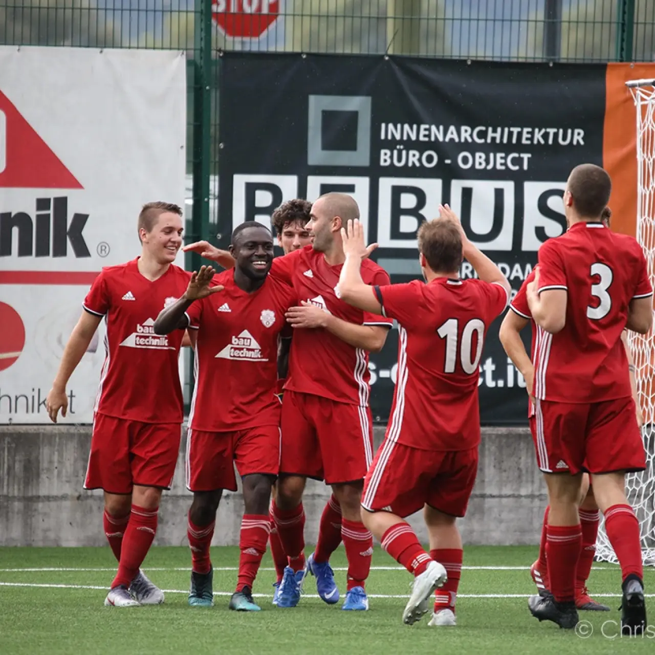 Rot gekleidete Spieler des AFC Terlan jubeln auf dem Kunstrasen, im Hintergrund Werbebanner von Bautechnik und einem Innenarchitekturbüro.