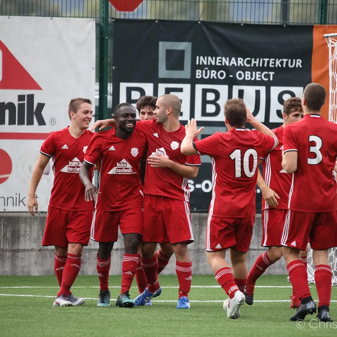 Rot gekleidete Spieler des AFC Terlan jubeln nach einem Treffer vor dem Tor, im Hintergrund Werbebanden von bautechnik und REBUS.