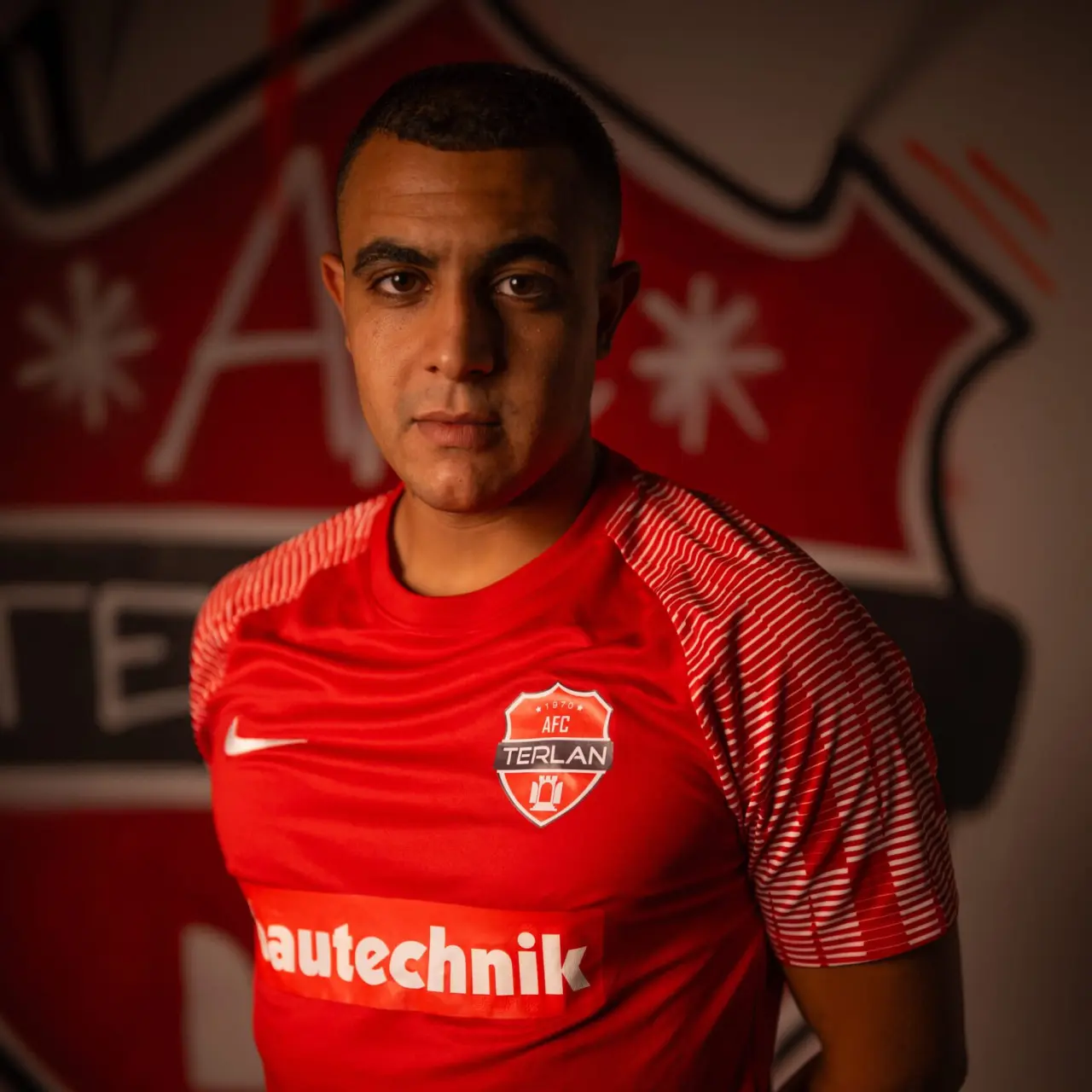 Porträt eines Spielers des AFC Terlan in roten Trikot mit Vereinswappen und Sponsor Bautechnik, vor einer roten Wand mit Vereinslogo.
