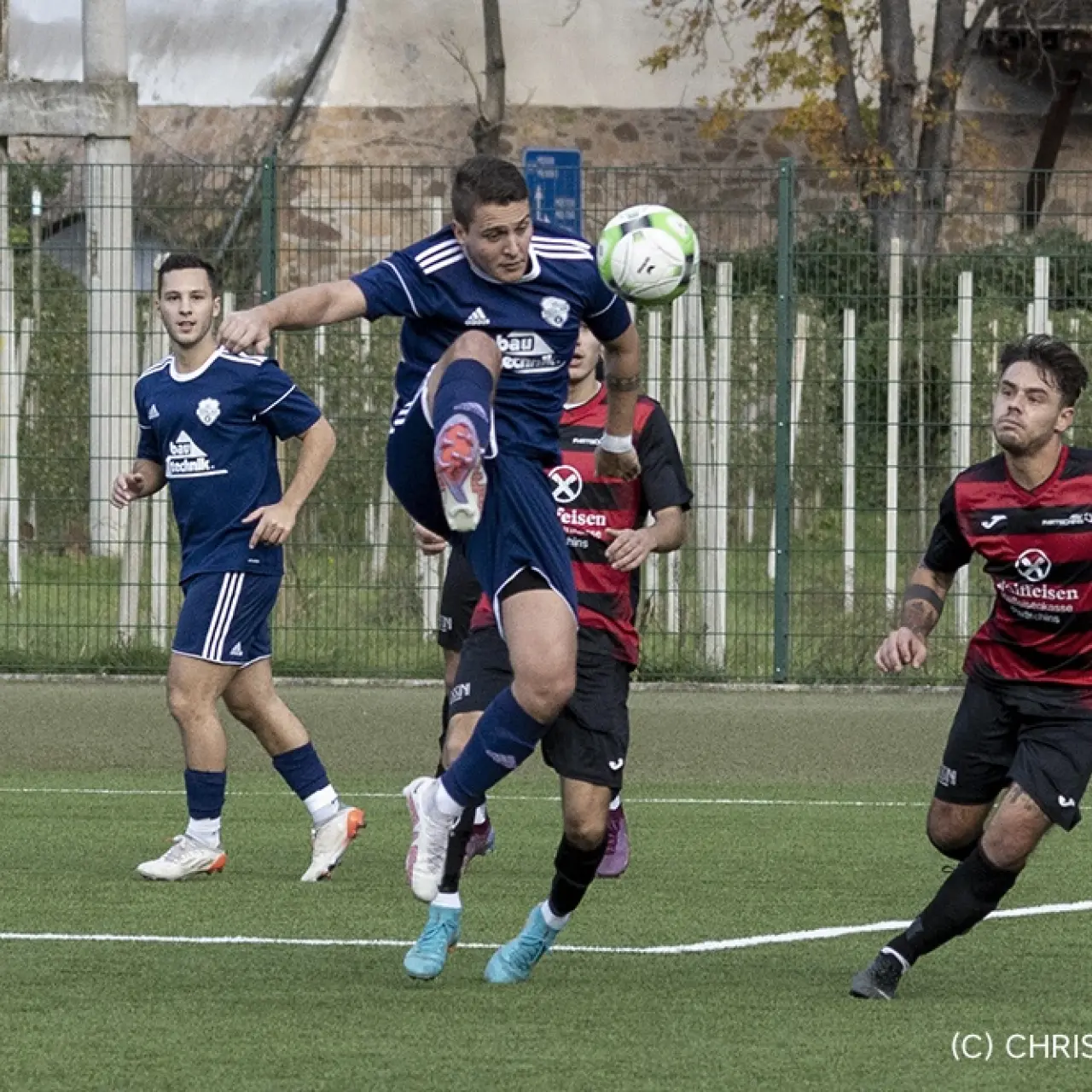 Spieler in blauem Trikot des AFC Terlan springt zum Ball, während ein Gegner in Rot-Schwarz und ein weiterer Terlaner zusehen.