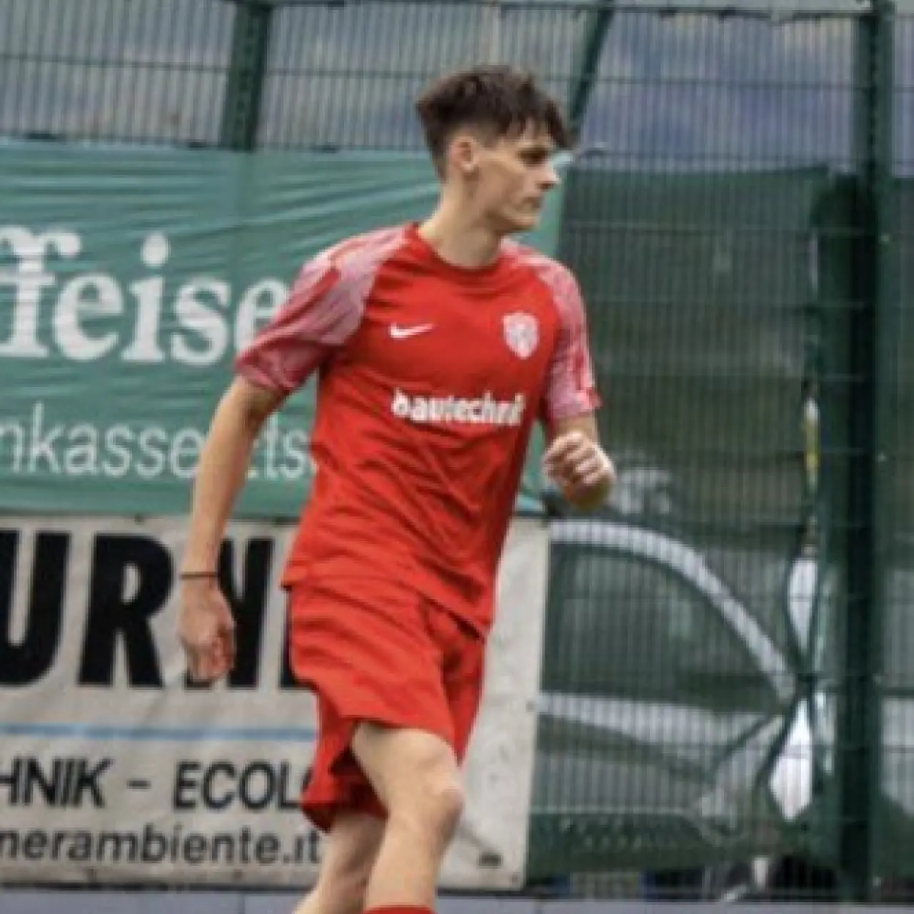Spieler in roter Trikotkombination führt den Ball am Spielfeldrand vor einer Bande mit Sponsorenwerbung.