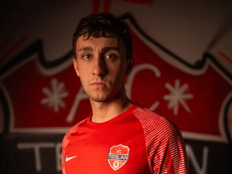 Spieler des AFC Terlan im roten Trikot mit Vereinswappen und Bautechnik-Sponsor, vor einer roten Wand mit dem Vereinslogo.