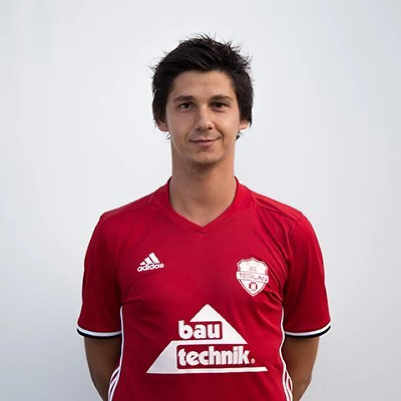 Porträtfoto von Mirza Cehaic im roten Trikot des AFC Terlan mit Bautechnik-Sponsorenaufdruck vor hellem Hintergrund.