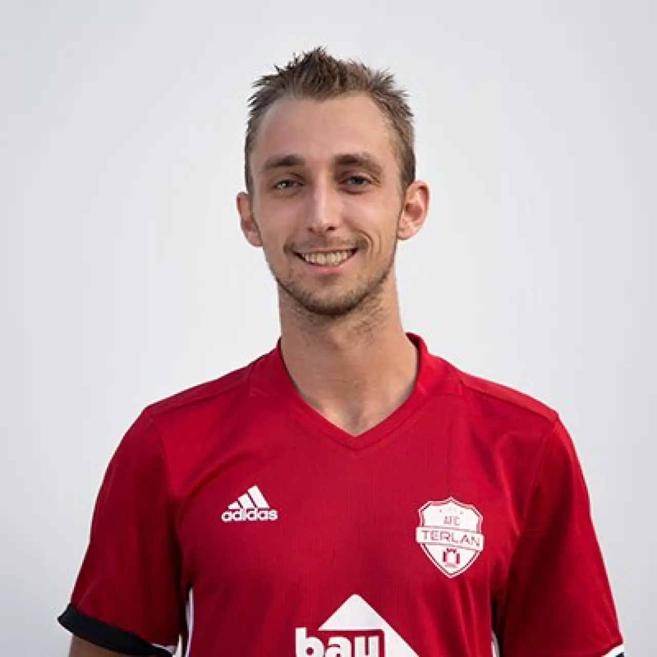 Porträtfoto eines lächelnden Spielers im roten Trikot des AFC Terlan mit Vereinswappen vor hellem Hintergrund.