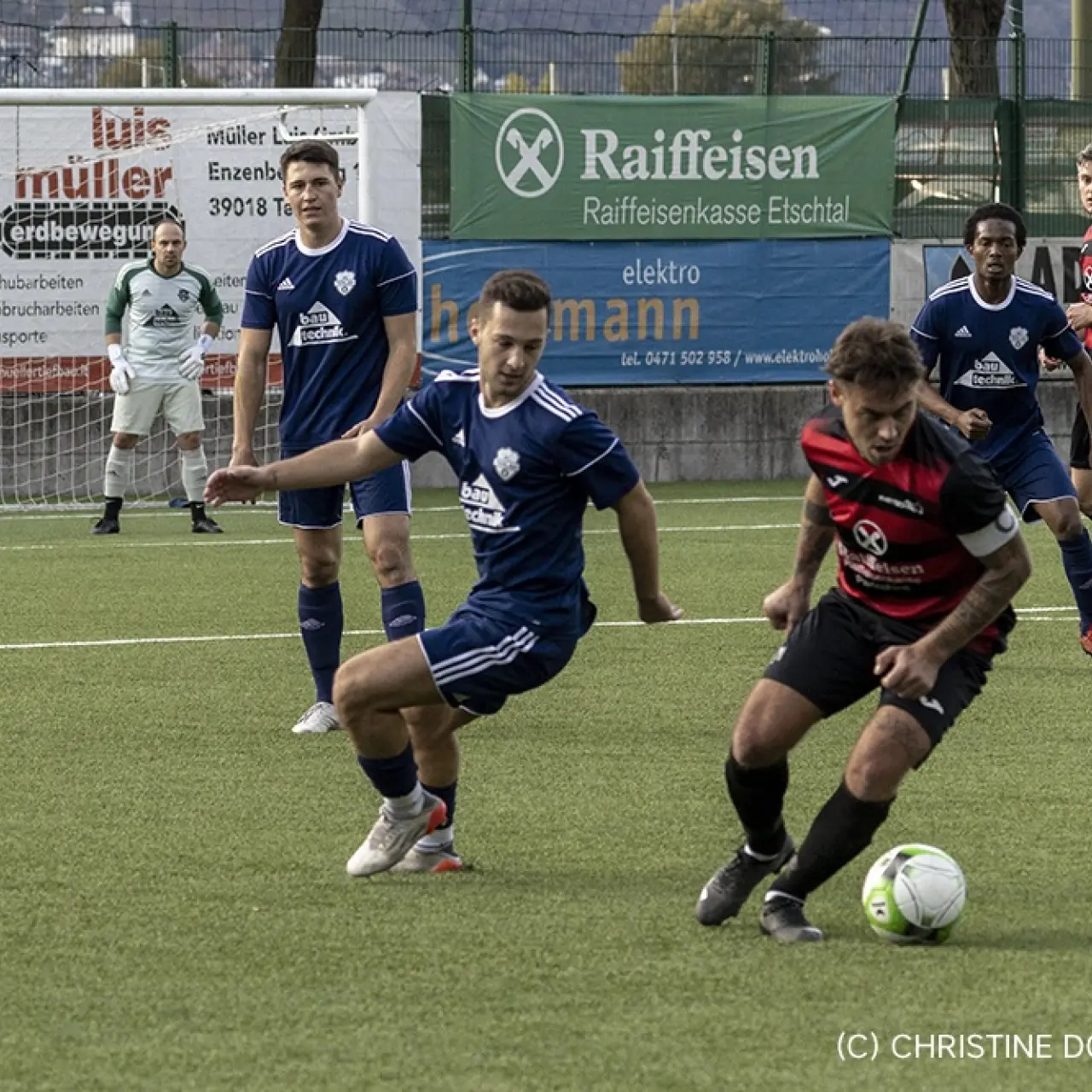 Spielszene: Ein Spieler in dunkelblauem Trikot des AFC Terlan stoppt den Ball gegen einen Gegner in Rot-Schwarz, Torwart im Hintergrund.