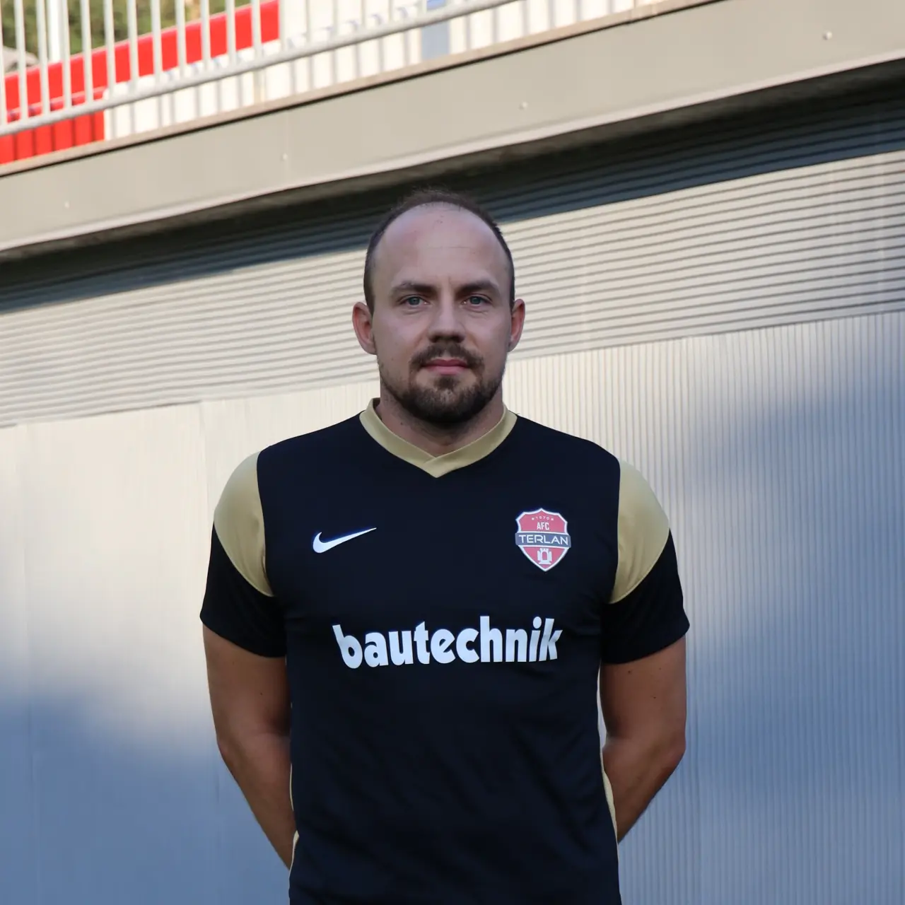 Porträtfoto von Lukas Malfatti vor einer grauen Wand im schwarzen AFC-Terlan-Trikot mit bautechnik-Sponsor.
