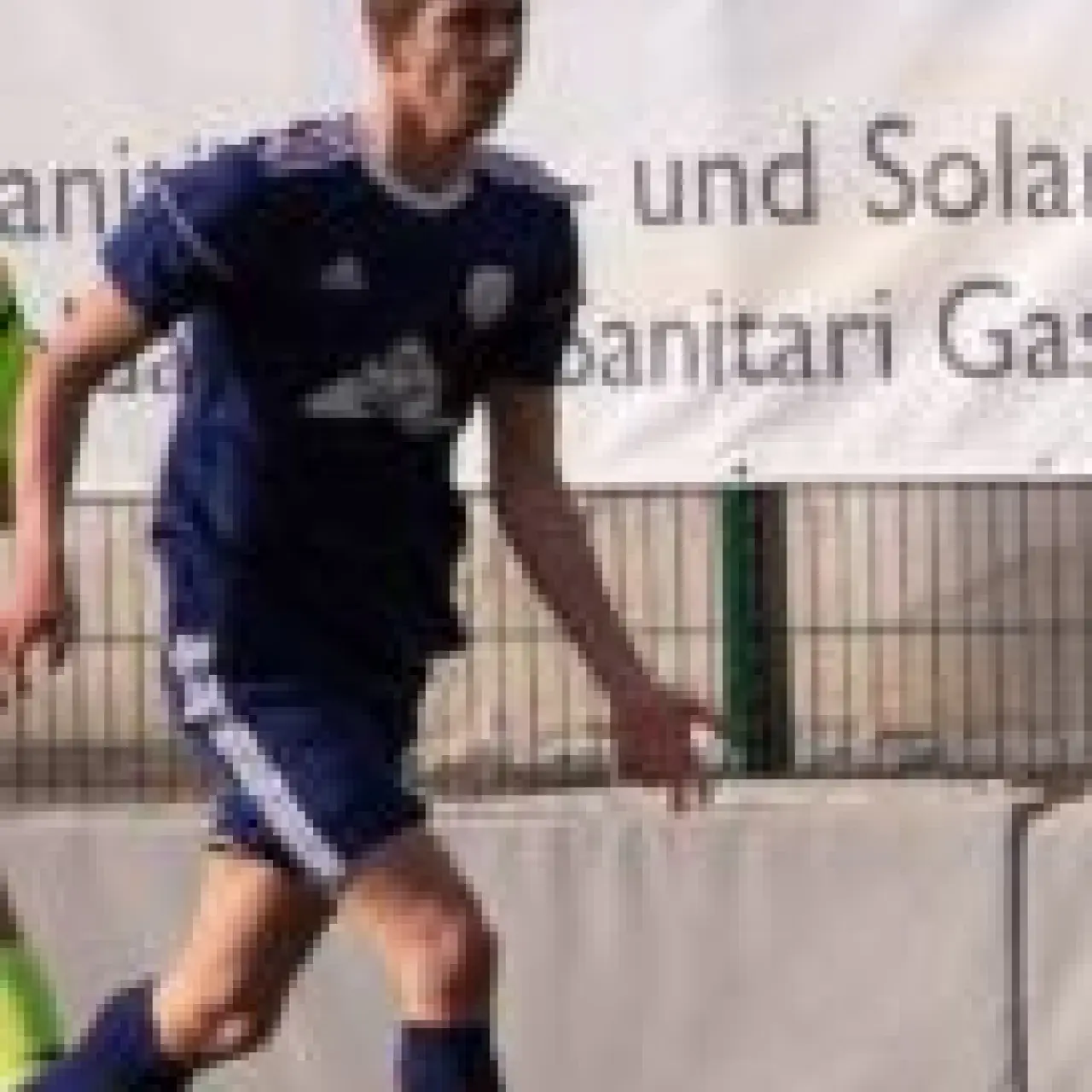 Spieler in blauem Trikot führt den Ball am Spielfeldrand, im Hintergrund Werbebanden mit Sponsorenschriftzug.