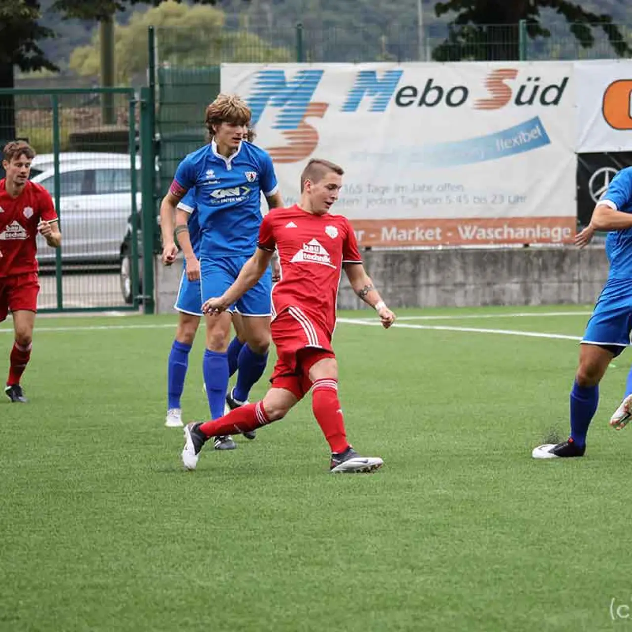 Spielszene: Ein Spieler in Rot schießt den Ball beim Spiel gegen Bruneck, während ein Gegenspieler in Blau am Ball ist.