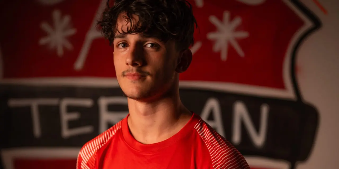 Junger Spieler im roten AFC-Terlan-Trikot mit Bautechnik-Sponsor vor dem bemalten Vereinswappen des AFC Terlan.