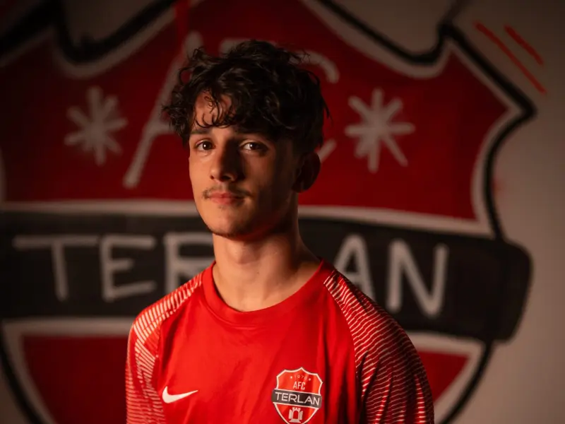 Junger Spieler im roten AFC-Terlan-Trikot mit Bautechnik-Sponsor vor dem bemalten Vereinswappen des AFC Terlan.