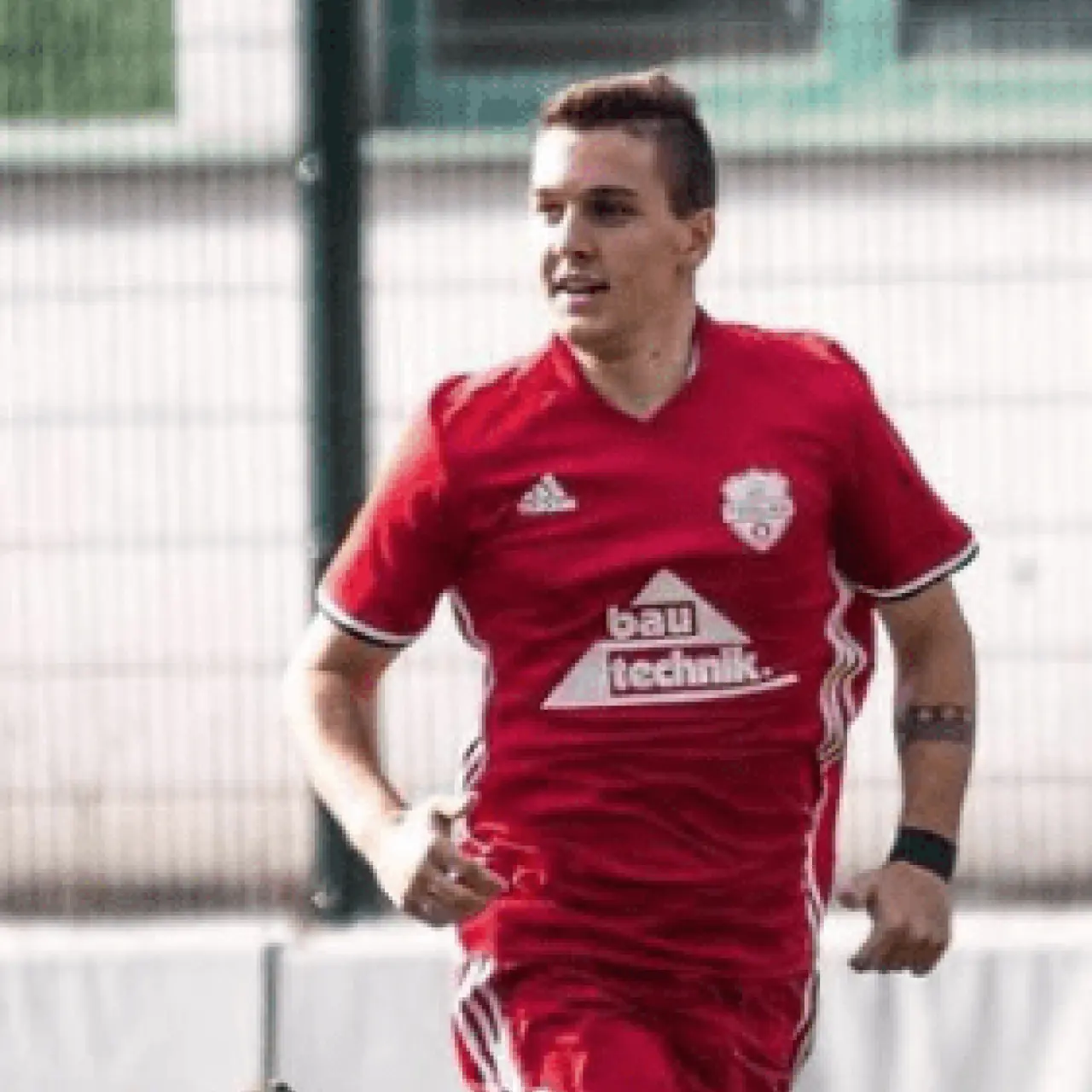 Spieler des AFC Terlan in roter Trikot mit bautechnik-Sponsorenlogo läuft auf dem Kunstrasen einem Ball nach.