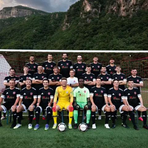 Mannschaftsfoto der Sturmtruppen des AFC Terlan in schwarzen Trikots mit Sponsorenaufdruck vor einem Tor, davor Berge.