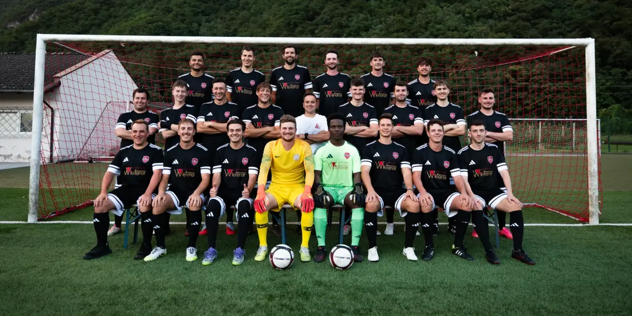 Mannschaftsfoto der Sturmtruppen des AFC Terlan in schwarzen Trikots mit Sponsorenaufdruck vor einem Tor, davor Berge.