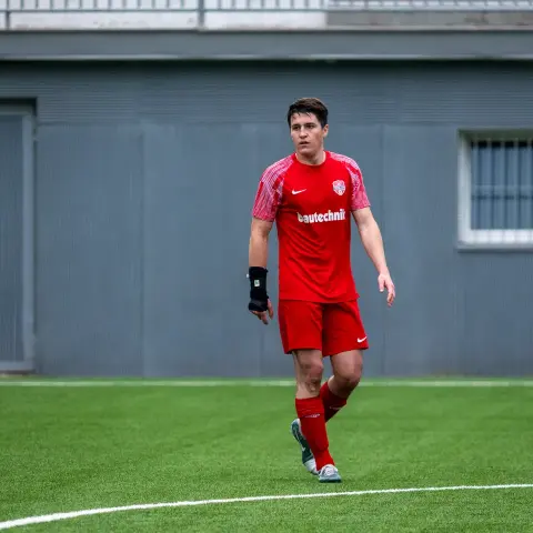 Spieler des AFC Terlan in roter Trikotkombi mit Bautechnik-Sponsor läuft über den Kunstrasenplatz, am linken Handgelenk eine schwarze Bandage.