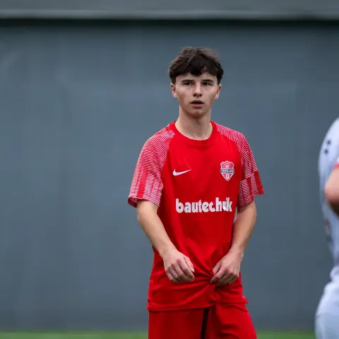 Ein junger Spieler im roten Trikot des AFC Terlan mit Bautechnik-Sponsor steht auf dem Platz und blickt aufmerksam zur Seite.