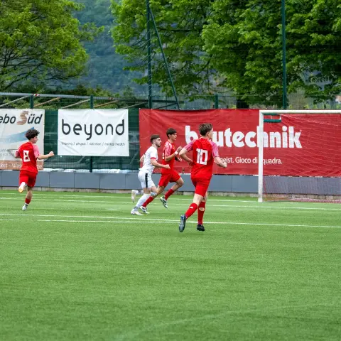 Spielszene auf dem Kunstrasen: Rote Trikots des AFC Terlan laufen einem Ball nach, im Hintergrund Bandenwerbung und der Torwart im Tor.