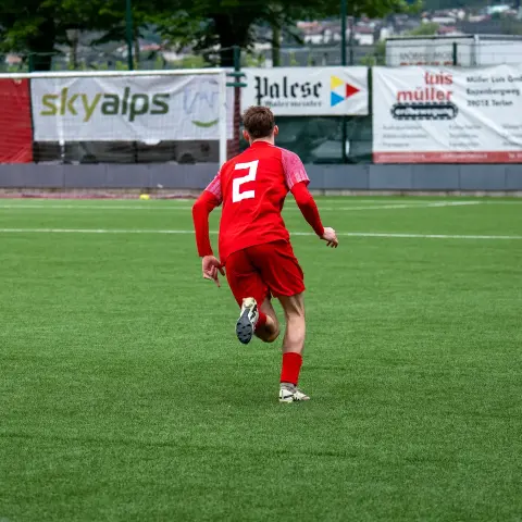 Spieler des AFC Terlan in roter Nummer 2 läuft über den Rasen, im Hintergrund Werbebanden und ein Torwart in dunkler Kleidung.