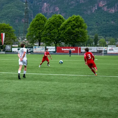 Fußball-Spielszene: Spieler in Rot und ein Spieler in Weiß kämpfen auf dem Kunstrasen um den Ball.