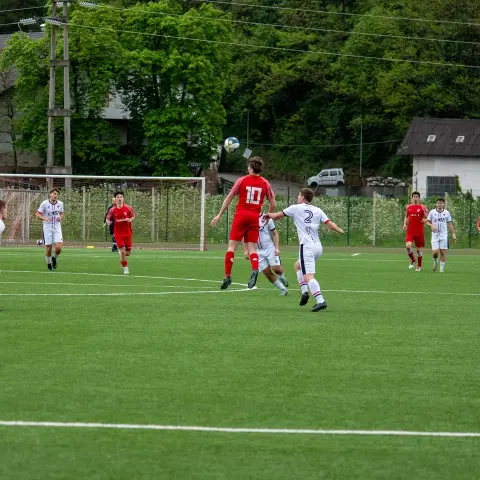 Spielszene: Spieler in Rot (Nummer 10) und in Weiß steigen gemeinsam zum Kopfball hoch auf dem Kunstrasen.
