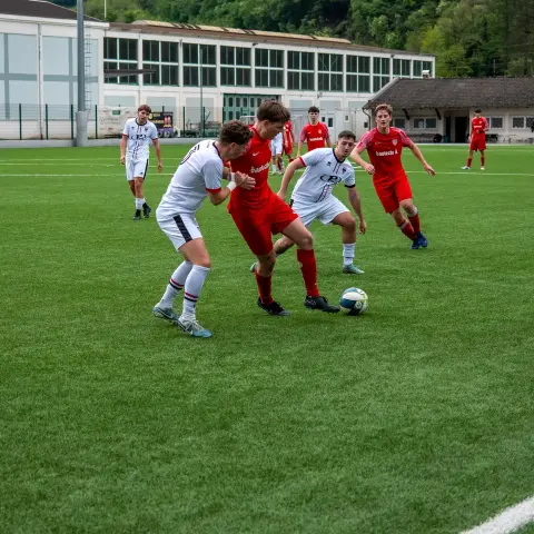 Zweikampf auf dem Kunstrasen: Spieler in Rot und Weiß kämpfen um den Ball, im Hintergrund weitere Spieler und Banden.