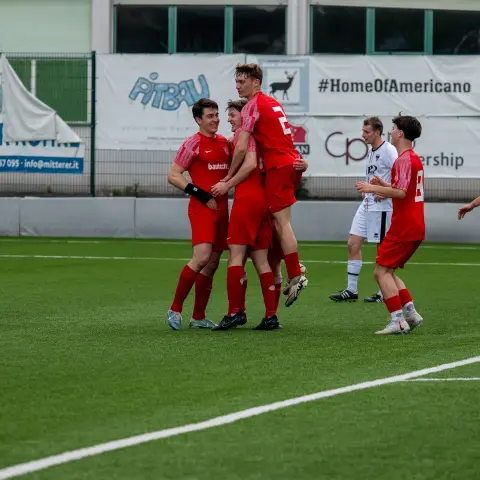 Rote Spieler des AFC Terlan jubeln nach einem Treffer auf dem Kunstrasen, mehrere umarmen sich, im Hintergrund stehen Gegner in Weiß.