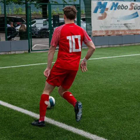 Spielszene: Spieler in rotem Trikot mit Nummer 10 führt den Ball am Seitenrand, ein Gegenspieler in Weiß läuft nach.