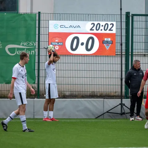 Spieler des AFC Terlan in Weiß holt den Ball zum Einwurf, daneben die Anzeigetafel mit 0:0 gegen A.S.D. Latsch.