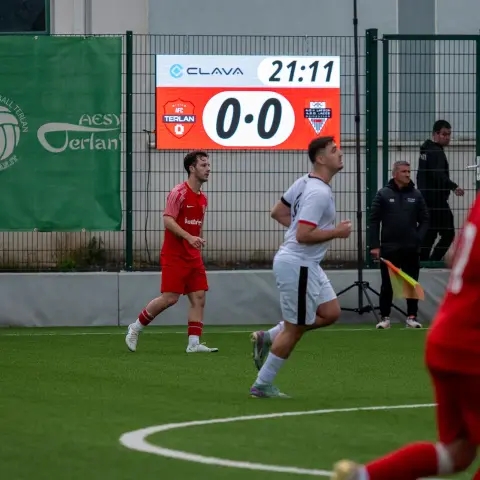 Spielszene: AFC Terlan in Rot gegen weiß gekleidete Gegner, die Anzeigetafel zeigt 0:0 in der 21. Minute.