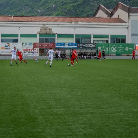Spielszene auf dem Kunstrasen: weiß und rot gekleidete Spieler kämpfen um den Ball vor Werbebanden, Anzeige steht auf 0:0.