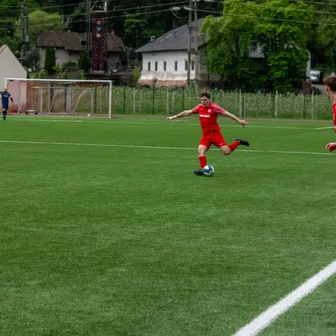 Ein roter Spieler des AFC Terlan schießt den Ball auf einem grünen Rasenplatz, im Vordergrund steht ein Mitspieler am Spielfeldrand.