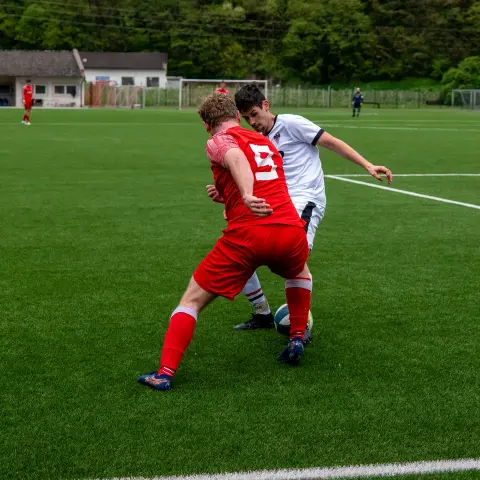 Zweikampf auf dem Kunstrasen: Ein Spieler in Rot mit der Nummer 8 deckt den Ball gegen einen Gegenspieler in Weiß ab.