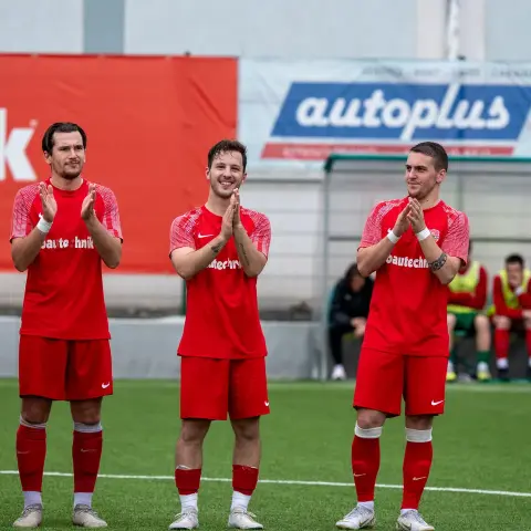 Vier Spieler des AFC Terlan in roten Trikots klatschen auf dem Rasen vor einer Bande, im Hintergrund Auswechselspieler mit Westen auf der Ersatzbank.