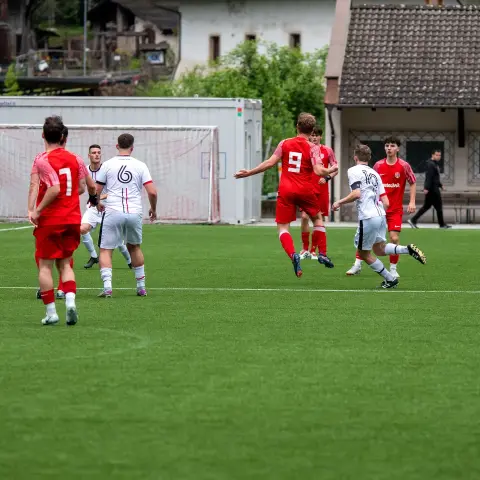 Spielszene auf dem Kunstrasen: Ein Spieler in Rot mit Nummer 9 läuft einem Ball nach, umringt von Spielern in Rot und Weiß.