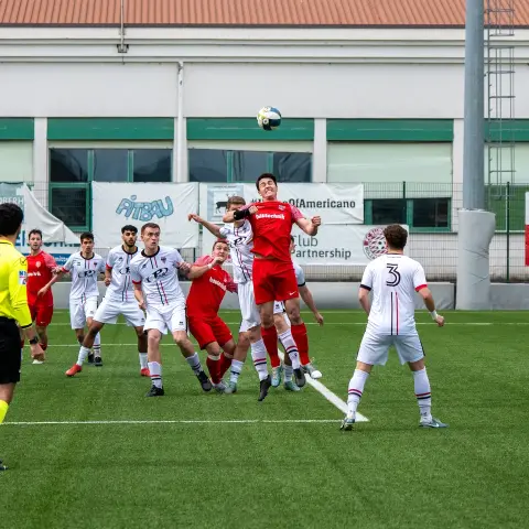 Kopfballduell in einem Spiel des AFC Terlan: Ein Spieler in Rot springt zum Ball, Gegner in Weiß drängen dazu.