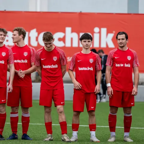 Sechs Spieler des AFC Terlan in roten Trikots mit bautechnik-Sponsorenaufdruck stehen nebeneinander auf dem Kunstrasen vor einer roten Bbande.