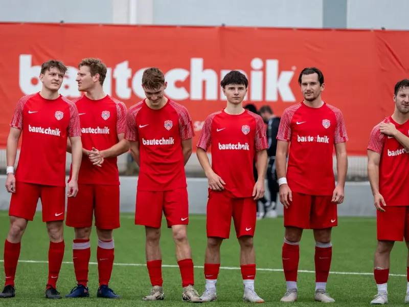 Sechs Spieler des AFC Terlan in roten Trikots mit bautechnik-Sponsorenaufdruck stehen nebeneinander auf dem Kunstrasen vor einer roten Bbande.